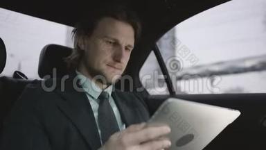 一个英俊的男人，棕色头发，穿着开心果衬衫，穿着灰色西装，坐在车用他的平板电脑工作